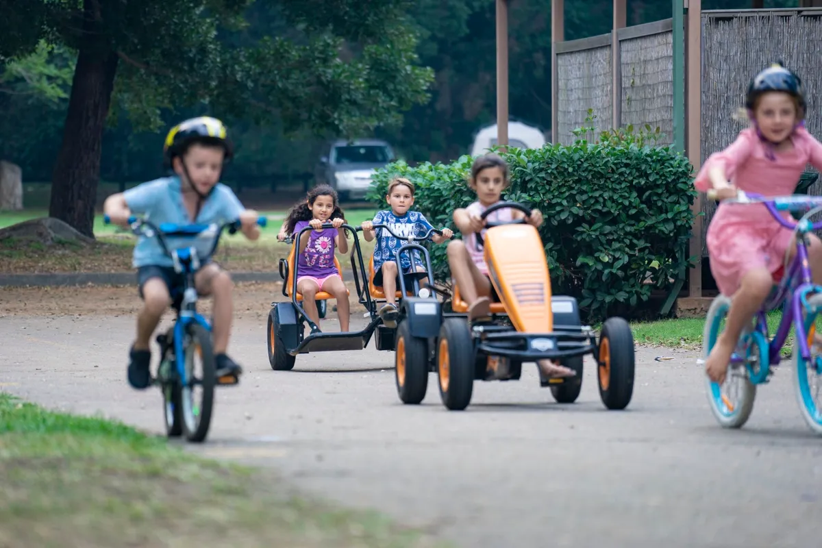 Children riding pedal karts and a bike along a path at Del Rio